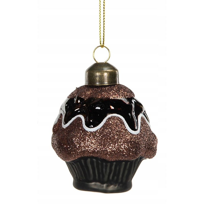 Zdjęcie produktowe typu packshot wykonane na jednolitym, białym tle. Przedstawia oryginalną, szklaną bombkę choinkową w kształcie smakowitej babeczki (cupcake'a). Dolna część ozdoby imituje ciemną, prążkowaną papilotkę, natomiast wypukła góra jest obficie obsypana brązowym brokatem, przypominając czekoladowe ciasto. Całość wieńczy lśniąca, ciemna "polewa" ozdobiona falistą, białą linią lukru. Na szczycie znajduje się metalowy kapselek ze złotym sznureczkiem do zawieszenia