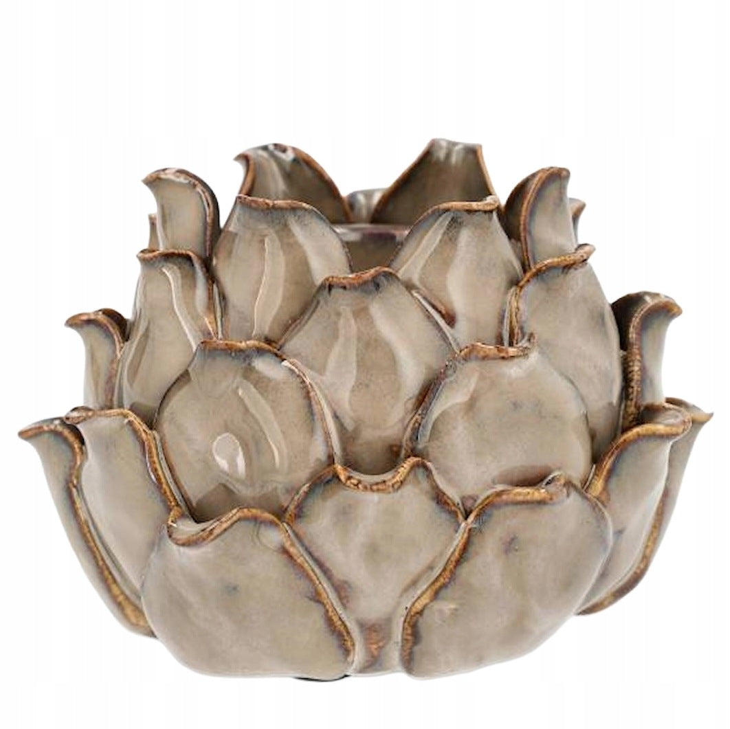 Zdjęcie produktowe na białym tle (packshot). Pękaty, ceramiczny świecznik przypominający swoim kształtem kwiat lotosu lub karczocha. Powierzchnia pokryta jest błyszczącym szkliwem w neutralnym, beżowo-szarym kolorze. Krawędzie łusek (płatków) mają ciemniejsze, brązowe przetarcia, które nadają naczyniu rustykalny, postarzany wygląd. Wewnątrz widoczne jest wgłębienie na świecę lub tealight.