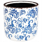 Pusta, cylindryczna donica (osłonka) ceramiczna o błyszczącym wykończeniu. Jej białą powierzchnię w całości pokrywa bogaty, niebieski ornament roślinny, nawiązujący do klasycznej majoliki lub holenderskich wzorów z Delft. Górna krawędź naczynia jest celowo postarzana – wykończona nierównym, ciemnobrązowym rantem imitującym rdzę i otarcia. Zdjęcie produktowe typu packshot wykonane na jednolitym, białym tle.