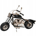 Zdjęcie produktowe na gładkim, białym tle (packshot). Metalowy model motocykla typu chopper oparty na bocznej stopce. Figurka posiada czarny bak paliwa, błotniki i opony, natomiast blok silnika, rama, układ wydechowy i wysoka kierownica z lusterkami wykończone są w kolorze przecieranego srebra. Model charakteryzuje się surowym, lekko postarzanym, industrialnym wyglądem.