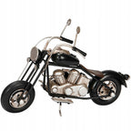 Zdjęcie produktowe na gładkim, białym tle (packshot). Metalowy model motocykla typu chopper oparty na bocznej stopce. Figurka posiada czarny bak paliwa, błotniki i opony, natomiast blok silnika, rama, układ wydechowy i wysoka kierownica z lusterkami wykończone są w kolorze przecieranego srebra. Model charakteryzuje się surowym, lekko postarzanym, industrialnym wyglądem.