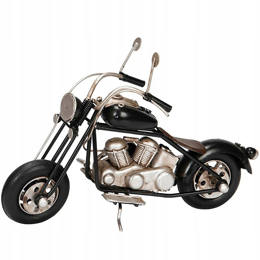 Zdjęcie produktowe na gładkim, białym tle (packshot). Metalowy model motocykla typu chopper oparty na bocznej stopce. Figurka posiada czarny bak paliwa, błotniki i opony, natomiast blok silnika, rama, układ wydechowy i wysoka kierownica z lusterkami wykończone są w kolorze przecieranego srebra. Model charakteryzuje się surowym, lekko postarzanym, industrialnym wyglądem.