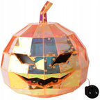 Zdjęcie produktowe na białym tle (packshot). Lampa w kształcie dyni na Halloween (tzw. Jack-o'-lantern) poskładana z geometrycznych paneli o holograficznym, pomarańczowo-różowym wykończeniu, odbijającym światło. Dynia posiada wycięte, groźne oczy i zębaty uśmiech. Z boku widoczny jest fragment czarnego kabla zasilającego z wtyczką.