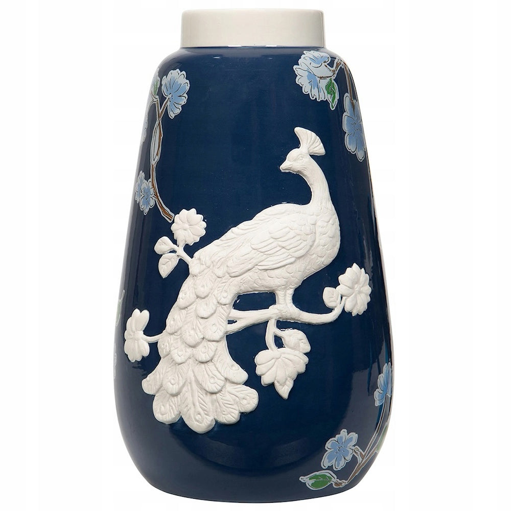 Ceramiczny wazon w kolorze głębokiego granatu z białą obwódką na górze. Główną ozdobą naczynia jest trójwymiarowy, biały relief przedstawiający pawia siedzącego na gałęzi. Tło wazonu uzupełniają subtelne, płaskie malowane błękitne kwiaty z zielonymi listkami. Zdjęcie produktowe typu packshot wykonane na jednolitym, białym tle