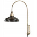 Zdjęcie produktowe na białym tle (packshot). Lampa ścienna (kinkiet) o surowym, industrialnym designie. Posiada ciemnobrązowy (rdzawy), metalowy klosz o spłaszczonym kształcie z elementami w kolorze antycznego mosiądzu. Ramię lampy jest długie, wygięte w łuk i osadzone w masywnym, prostokątnym uchwycie ściennym, umożliwiającym regulację jej wysokości za pomocą pokrętła.