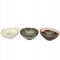 Zestaw trzech małych miseczek ceramicznych o organicznym, asymetrycznym kształcie. Każda miseczka pokryta jest unikalnym szkliwem reaktywnym, tworzącym zachwycające, wielobarwne efekty wewnątrz naczyń (jasnoseledynowy, głęboki turkus oraz ciemny brąz z zielenią). Zewnętrzne krawędzie wykończono rustykalnym, brązowym rantem. Zdjęcie produktowe typu packshot wykonane na czystym, białym tle, w pełni oddające głębię kolorów i rzemieślniczy charakter ceramiki.