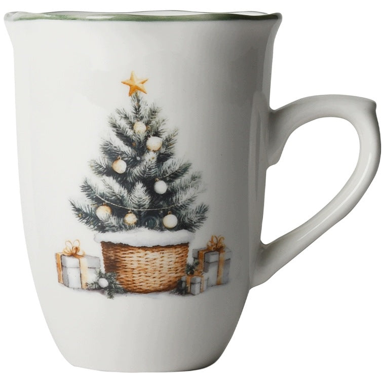 Zdjęcie produktowe na gładkim, białym tle (packshot). Przedstawia smukły, ceramiczny kubek z wygodnym uchem i profilowanym rantem wykończonym ciemnozieloną linią. Na ściance kubka znajduje się nastrojowy nadruk ośnieżonej choinki w plecionym koszu, ze złotą gwiazdą na czubku oraz ułożonymi u dołu prezentami z kokardami.