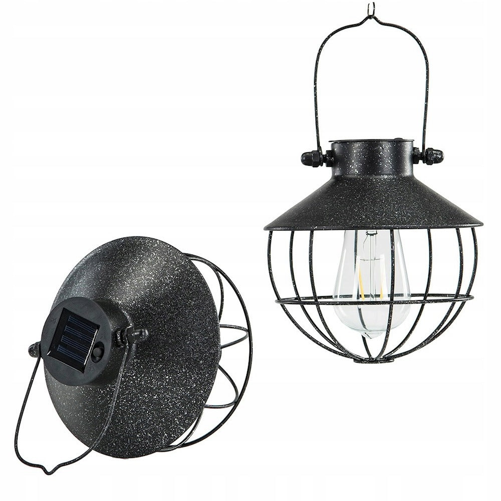 Zdjęcie produktowe na białym, czystym tle (packshot). Zestawienie dwóch rzutów na wiszącą lampę solarną w stylu loftowym. Lampa z prawej strony wisi prosto na metalowym uchwycie, ukazując przypominający dzwonek kloszyk, drucianą osłonę oraz stylizowaną żarówkę LED. Lampa z lewej strony jest pochylona, aby wyraźnie wyeksponować górną część klosza, gdzie zamontowany jest niewielki, kwadratowy panel słoneczny oraz przycisk zasilania. 