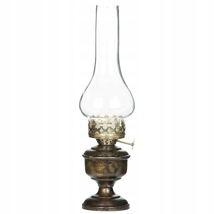 Zdjęcie produktowe na gładkim, białym tle (packshot). Lampion na świeczkę typu tealight, zaprojektowany na wzór tradycyjnej lampy naftowej. Posiada profilowaną podstawę w kolorze postarzanego mosiądzu, ozdobną metalową galeryjkę oraz charakterystyczny, pękaty u dołu i zwężający się ku górze szklany komin (klosz).