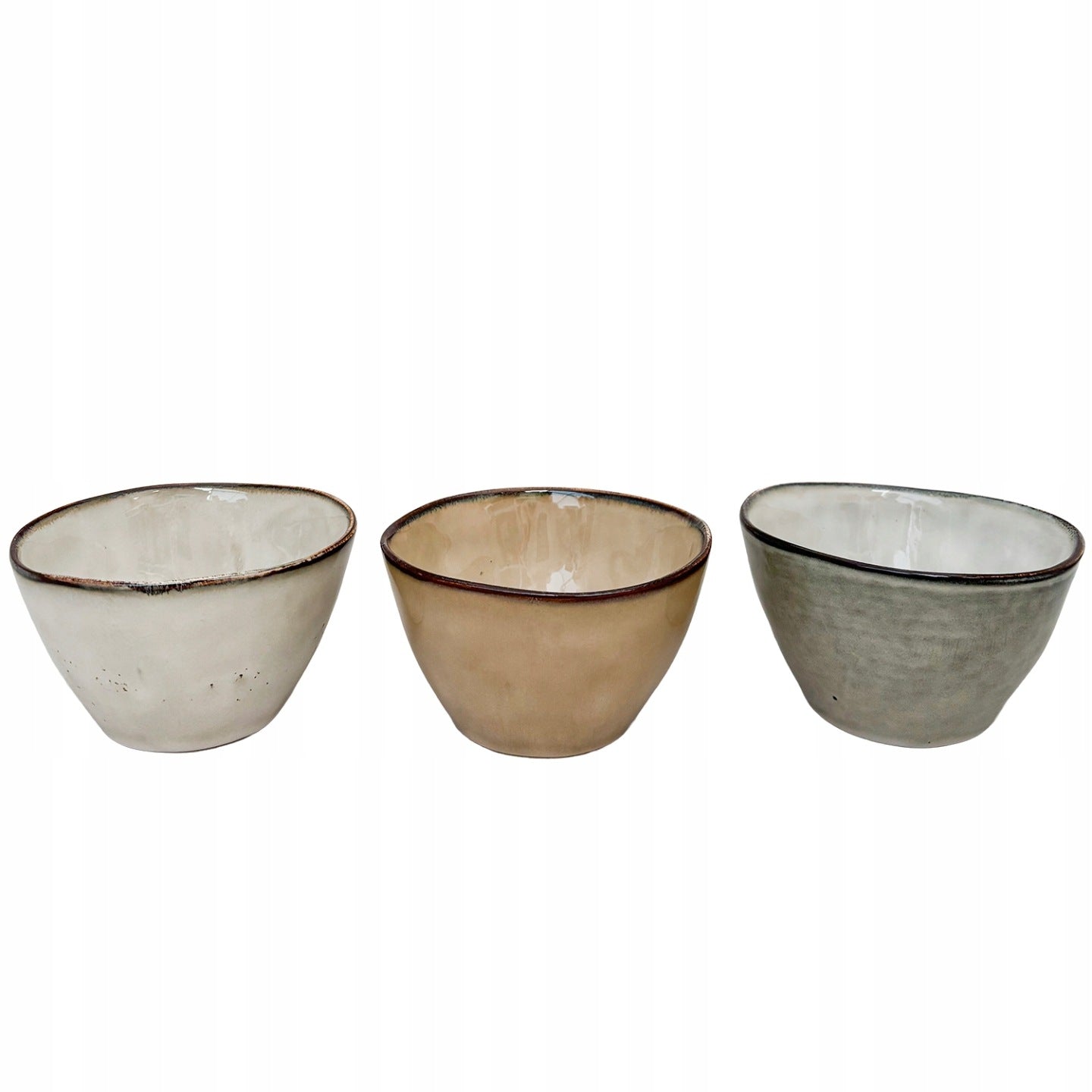 Zestaw trzech małych miseczek ceramicznych o organicznym, lekko nieregularnym kształcie, przypominającym rękodzieło. Naczynia pokryte są błyszczącym szkliwem w trzech stonowanych barwach: kremowej, beżowej oraz szaro-zielonej. Brzegi wykończono kontrastującym, ciemnym rantem, który nadaje im charakteru. Zdjęcie produktowe typu packshot wykonane na jednolitym, białym tle, doskonale prezentujące kolory i lśniącą fakturę.