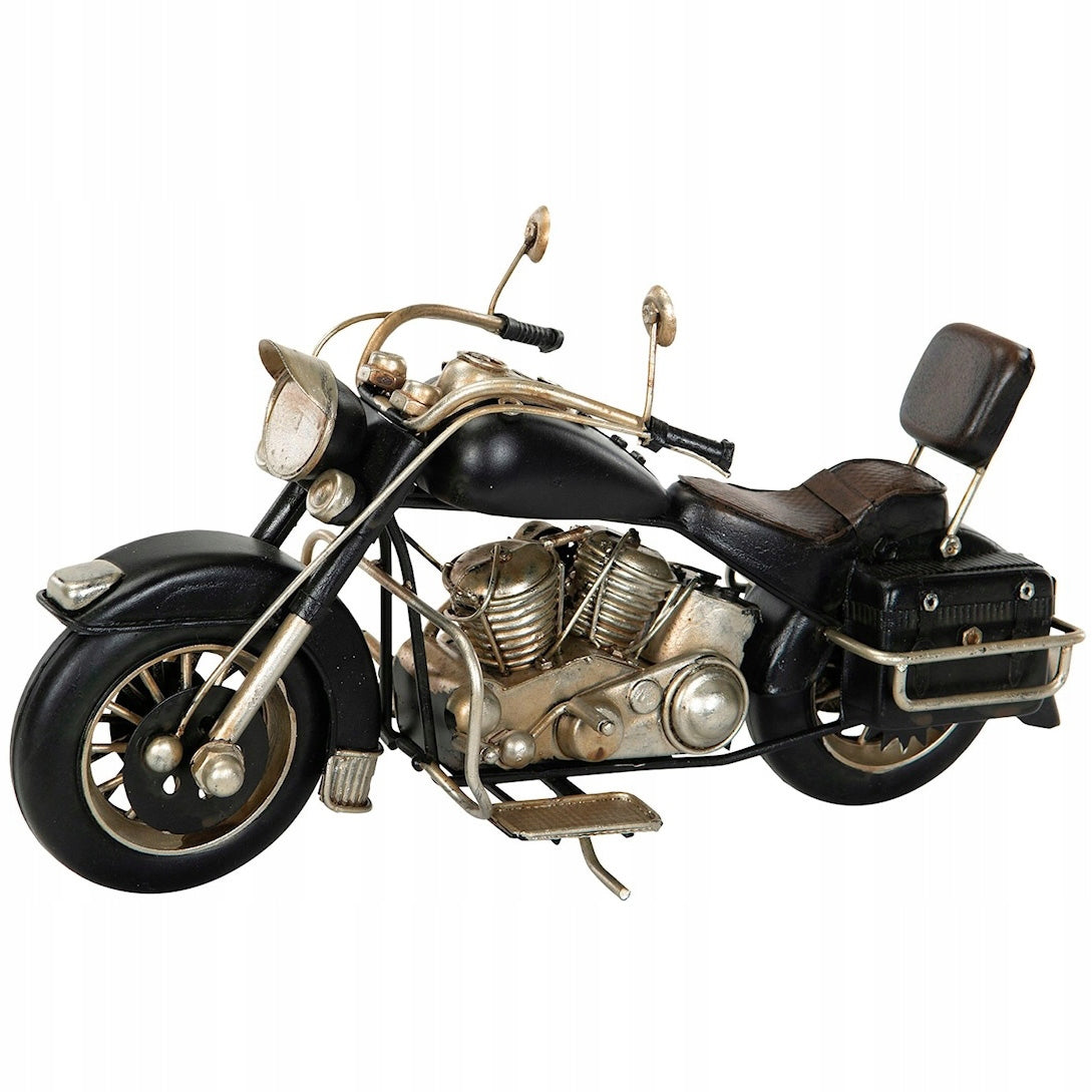 Zdjęcie produktowe na białym, gładkim tle (packshot). Dekoracyjny, metalowy model klasycznego motocykla (chopper) w kolorze czarnym z widocznymi srebrnymi i miedzianymi elementami silnika oraz układu wydechowego. Model ma szczegółowo oddane detale, takie jak skórzane siedzenie, oparcie dla pasażera, boczne sakwy, duże okrągłe przednie światło i lusterka. Ustawiony jest na wysuwanej nóżce.