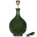 Ceramiczna podstawa lampy stołowej o eleganckim kształcie pękatej butli. Powierzchnia wykończona jest ciemnozielonym, lśniącym szkliwem z subtelnym cieniowaniem. Na górze zamontowana jest mosiężna oprawka z gwintem na żarówkę, a u dołu po prawej stronie widoczny jest czarny przewód zasilający z włącznikiem ręcznym i wtyczką. Zdjęcie produktowe typu packshot wykonane na jednolitym, białym tle.