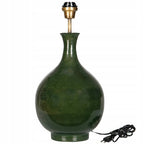 Ceramiczna podstawa lampy stołowej o eleganckim kształcie pękatej butli. Powierzchnia wykończona jest ciemnozielonym, lśniącym szkliwem z subtelnym cieniowaniem. Na górze zamontowana jest mosiężna oprawka z gwintem na żarówkę, a u dołu po prawej stronie widoczny jest czarny przewód zasilający z włącznikiem ręcznym i wtyczką. Zdjęcie produktowe typu packshot wykonane na jednolitym, białym tle.