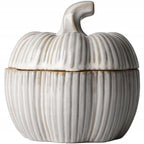 Zdjęcie produktowe na białym tle (packshot). Kremowe, ceramiczne naczynie z przykrywką w kształcie dyni. Powierzchnia ozdobiona jest wyraźnymi, pionowymi prążkami (ryflowaniem) i pokryta lśniącym szkliwem. Na krawędziach i wgłębieniach widoczne są delikatne, brązowe przetarcia nadające całości rustykalny charakter. Pokrywka zwieńczona jest profilowanym, zaokrąglonym ogonkiem.