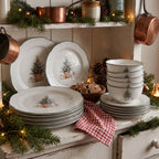 Świąteczna ekspozycja kompletu naczyń ceramicznych na białym, stylizowanym kredensie kuchennym. Na blacie ułożono stosy dużych talerzy obiadowych, talerzy deserowych oraz piramidę miseczek z motywem ubranej choinki w koszu. Dwa talerze wyeksponowano pionowo na ściance kredensu. Całość uzupełniają gałązki świerku z lampkami choinkowymi, czerwona ściereczka w kratkę, miseczka z pierniczkami oraz wiszące u góry miedziane rondelki.