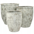 Zdjęcie produktowe na gładkim, białym tle (packshot). Zestaw trzech donic o różnych rozmiarach, wykonanych z materiału imitującego stary, przecierany kamień lub ceramikę. Donice mają jasnoszary kolor z licznymi, nieregularnymi brązowymi plamkami rdzy i patyny. Powierzchnia naczyń ozdobiona jest pionowymi, wypukłymi pasami oraz subtelnymi, roślinnymi i geometrycznymi ornamentami przy górnej krawędzi.